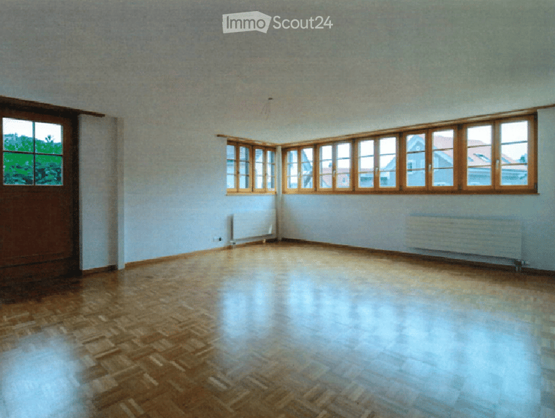 Empty room with wooden flooring, large windows, and radiators on the walls.