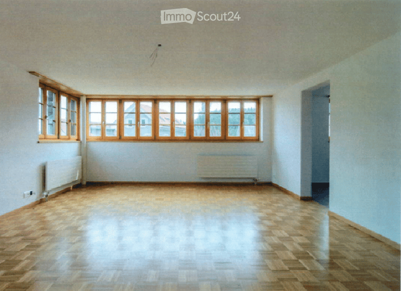 Empty room with wooden flooring, white walls, large windows with wooden frames, and radiators on both sides.