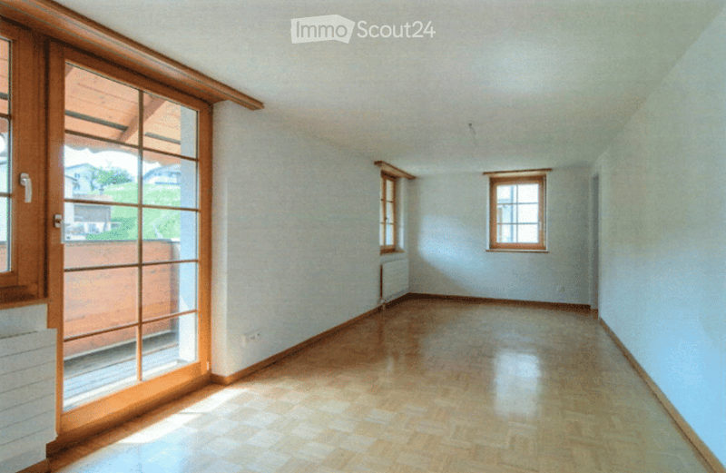 Empty room with wooden flooring, white walls, and large windows, including a sliding glass door leading to an outdoor area.