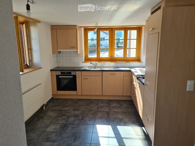 Modern kitchen with light wooden cabinets, dark tiled floor, and large windows. Features an oven, sink, and faucet.