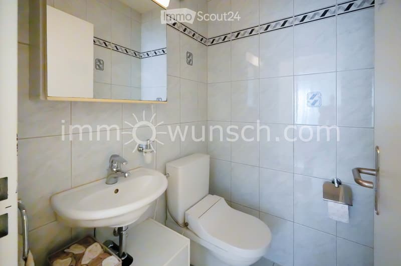 Modern bathroom with white tiles, a sink, toilet, mirror, and cabinet.