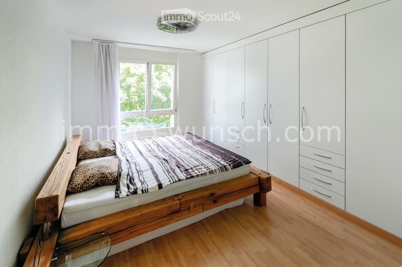 Modern bedroom with a wooden bed frame, striped bedding, leopard-print pillows, white built-in wardrobes, and large windows with curtains.