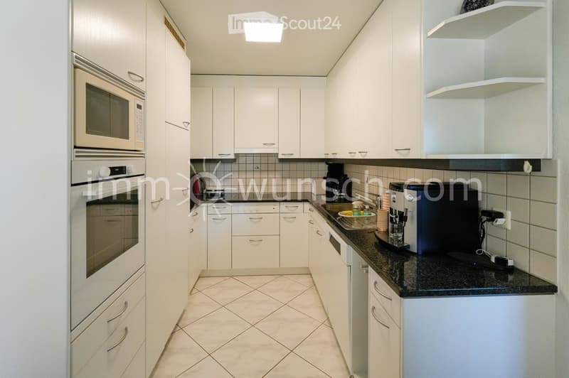 Modern kitchen with white cabinets, granite countertop, microwave, oven, coffee machine, and sink.