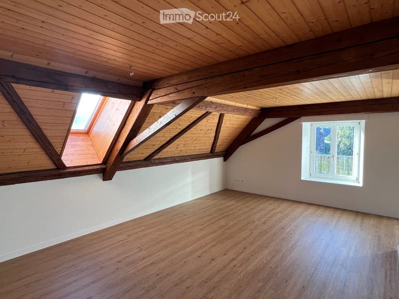 Empty attic room with wooden beams, skylight, and wooden flooring.