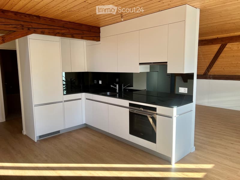 Modern kitchen with white cabinets, black countertop, stainless steel sink and faucet, and built-in oven. Wooden ceiling beams and light wooden flooring.