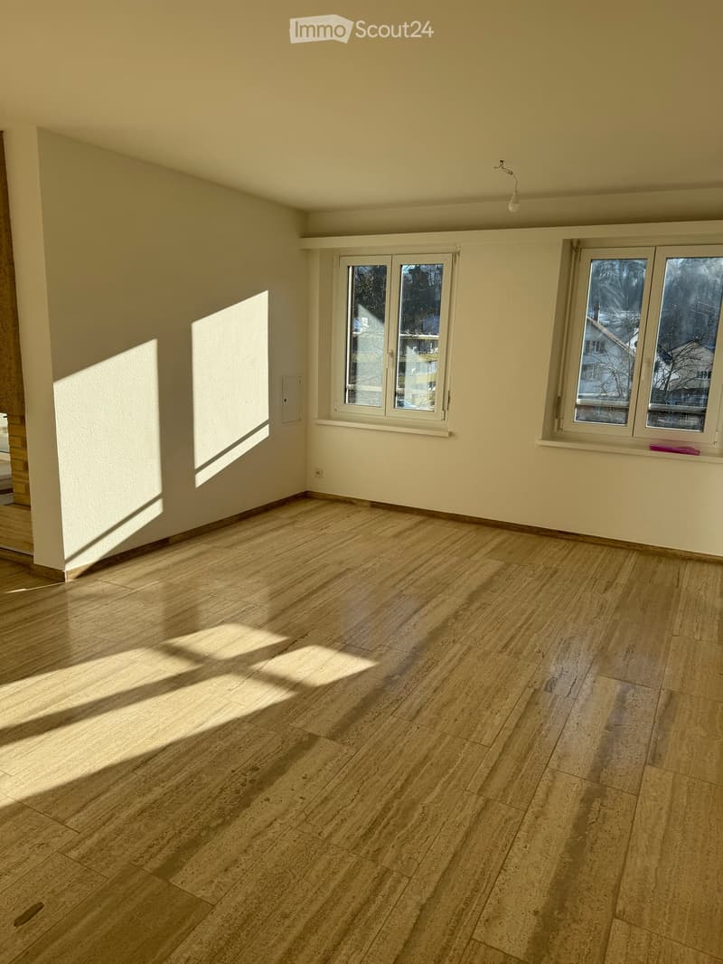 Empty room with light wooden flooring, white walls, and large windows allowing natural light to enter. The space is completely unfurnished with no visible furniture or equipment.