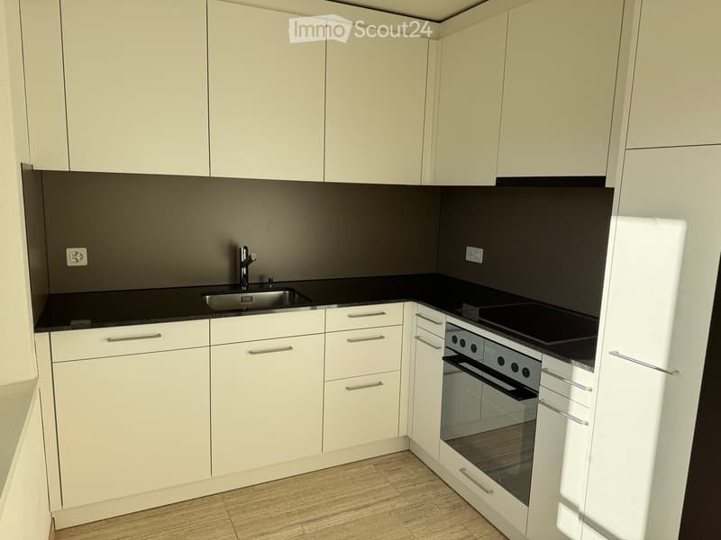 modern white kitchen with black countertops, silver sink, faucet, modern white cabinetry, oven, stove