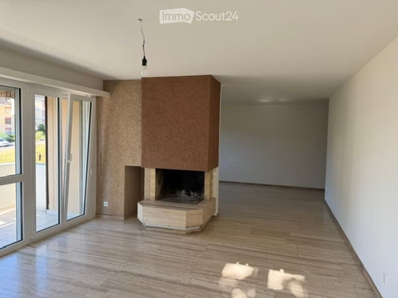Empty room with wooden flooring, white walls, large glass doors, and a built-in fireplace with a stone base and wooden mantel.