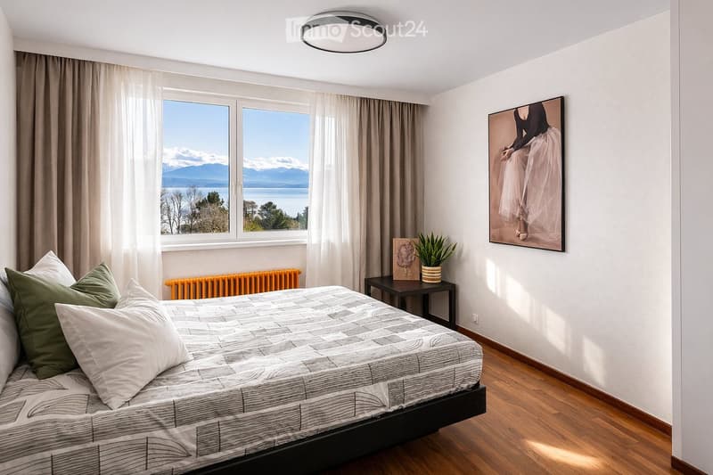 Modern bedroom with a large bed, green and white pillows, nightstand with a potted plant, artwork on the wall, and a scenic view of mountains and water through large windows.