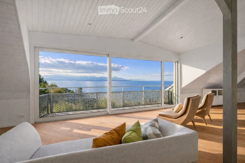 Bright living room with large windows offering a scenic ocean view, featuring a grey sofa with colorful pillows, a modern chair, and a sleek white cabinet.