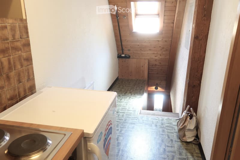Small kitchen area with white countertop, fridge, tile floor, wooden cabinet, and an open window on the wooden wall.