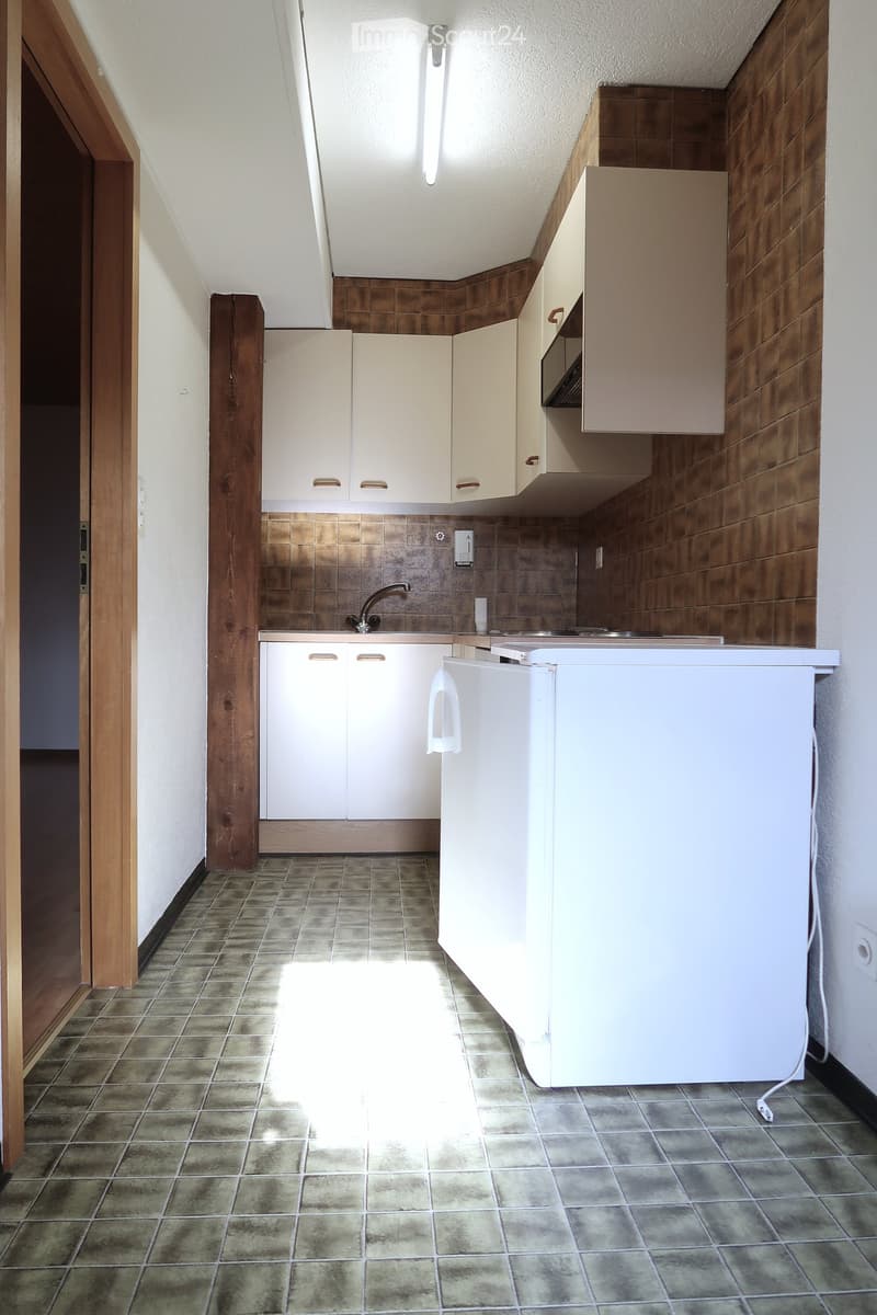 white tiled floor, white tiled walls, wooden cabinets, countertop, sink with faucet, small refrigerator, electrical outlet
