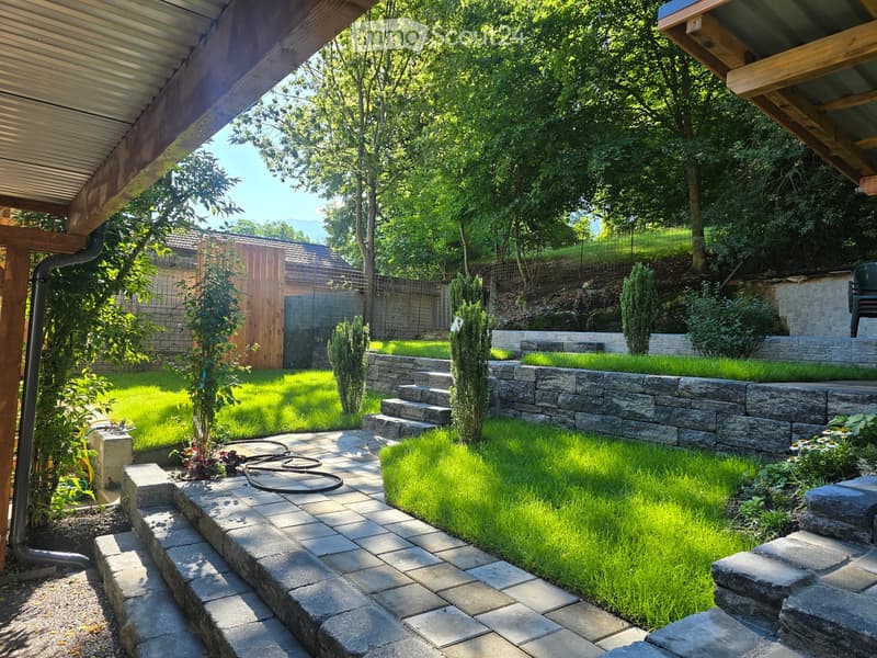 Well-maintained garden with stone steps, lush green grass, small trees, and a wooden fence in the background.