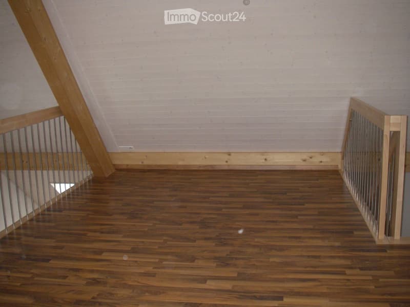 Empty room with wooden flooring, white walls, and a wooden staircase with metal railings.