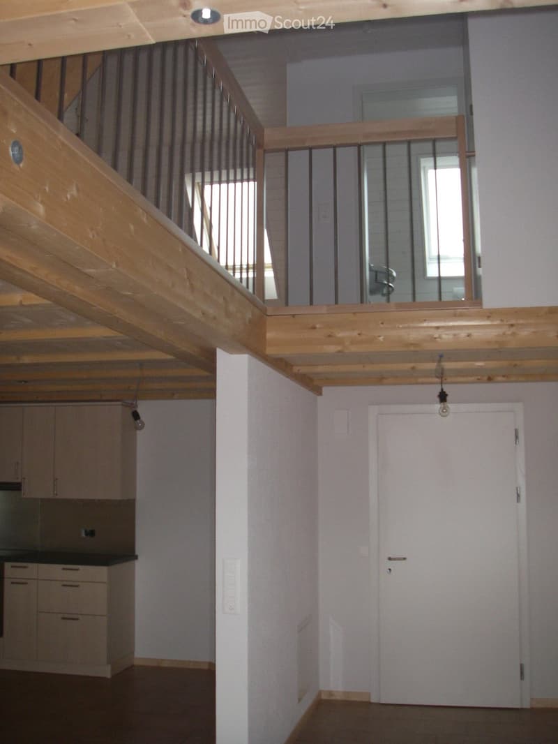 Empty hallway with wooden staircase leading to an upper level, white walls, and a closed door at the end.