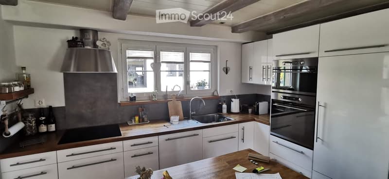 Modern kitchen with white cabinets, stainless steel appliances, wooden countertops, and a large window. Features include a sink, faucet, oven, refrigerator, and various kitchen items on the counter.