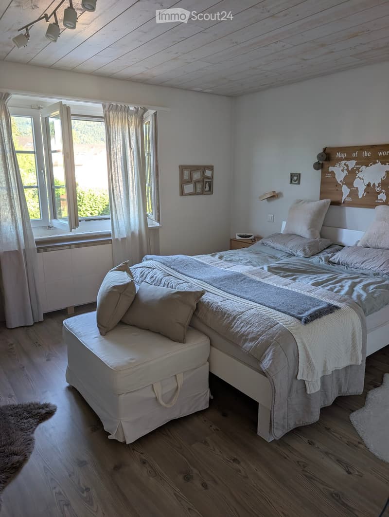 Cozy bedroom with a large bed, pillows, blanket, nightstand, world map on the wall, picture frame, and curtains on the windows.