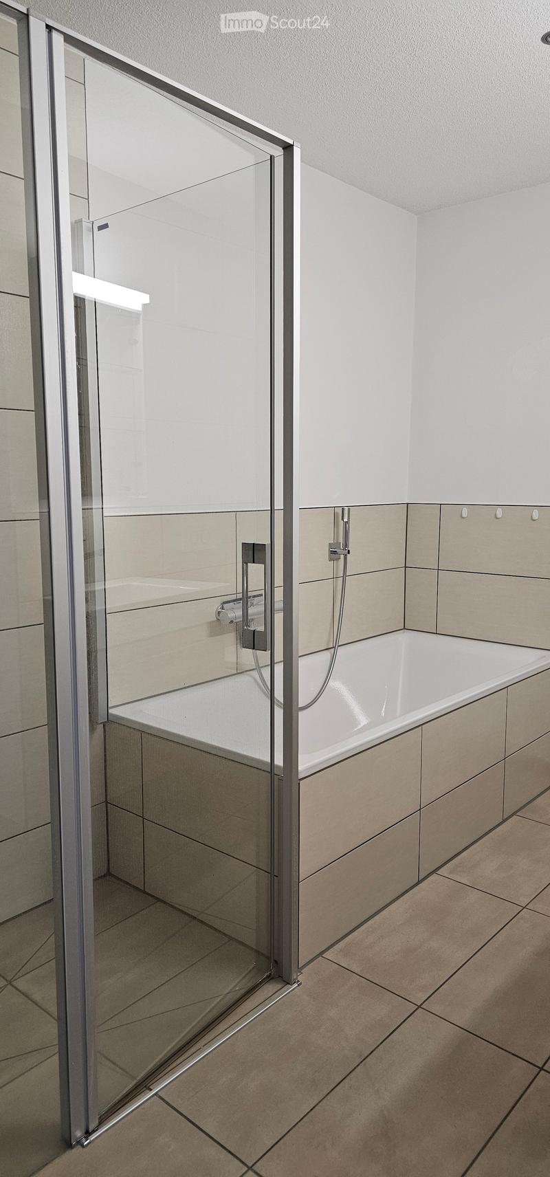 Modern bathroom with a bathtub, glass shower enclosure, and tiled walls and floor.