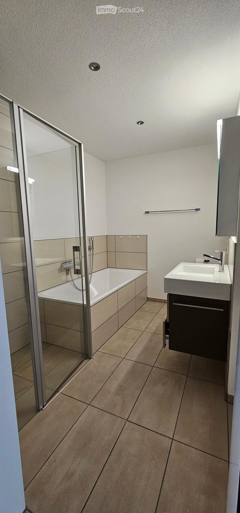 Modern bathroom with a bathtub, sink, mirror, and cabinet. Features tiled walls and floor, glass shower enclosure, and modern fixtures.
