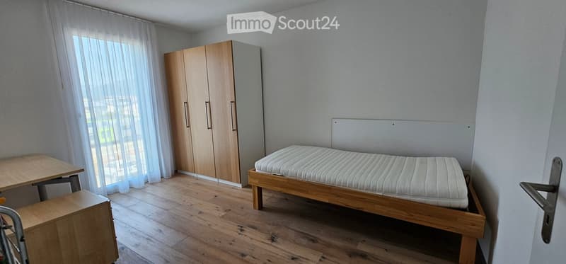 A small, modern bedroom with a wooden bed, a wardrobe, and a small table near the window.
