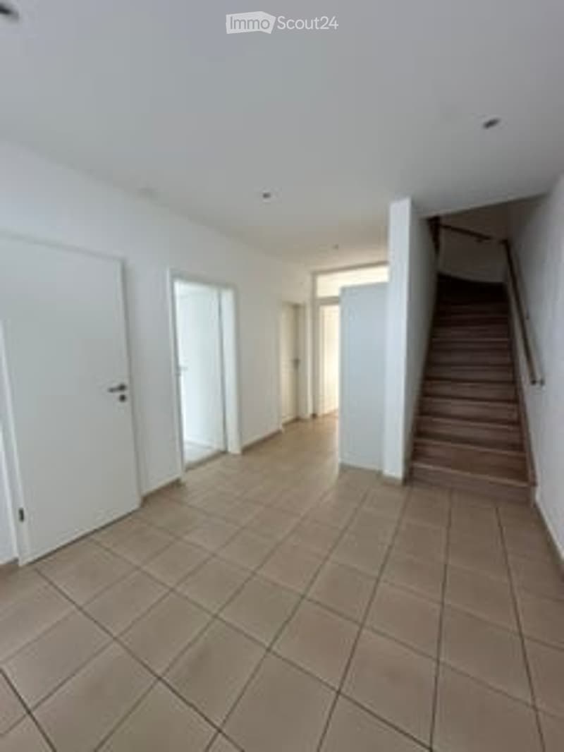 Empty room with tiled floor, white walls, and a staircase leading upwards.