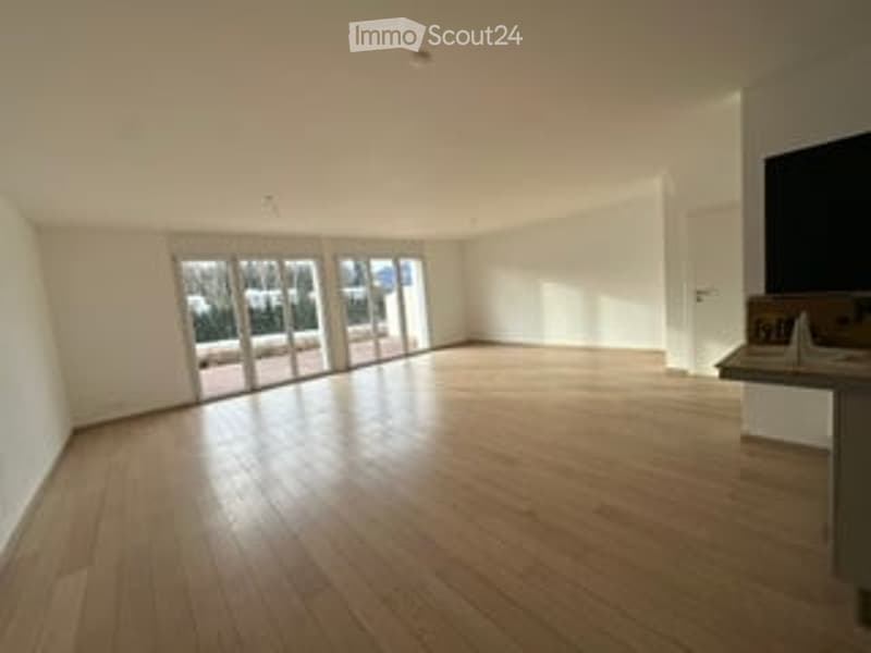 Bright, unfurnished room with large glass doors leading to a balcony, wooden flooring, and white walls.