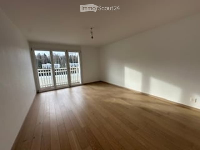 Empty room with wooden flooring, white walls, large sliding glass door leading to an outdoor area, and natural light streaming in.