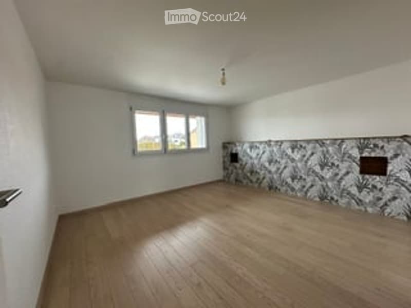 Empty room with wooden flooring, white walls, and a window with multiple panes. The room features a decorative tile backsplash on one wall.