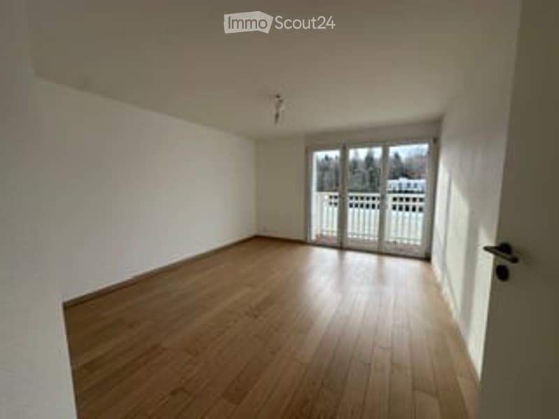 Completely empty room with wooden flooring, white walls, and large sliding glass doors leading to a balcony.