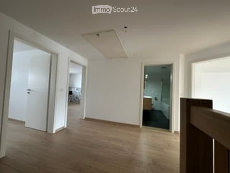 Empty room with wooden flooring, white walls, and multiple doorways leading to other rooms.