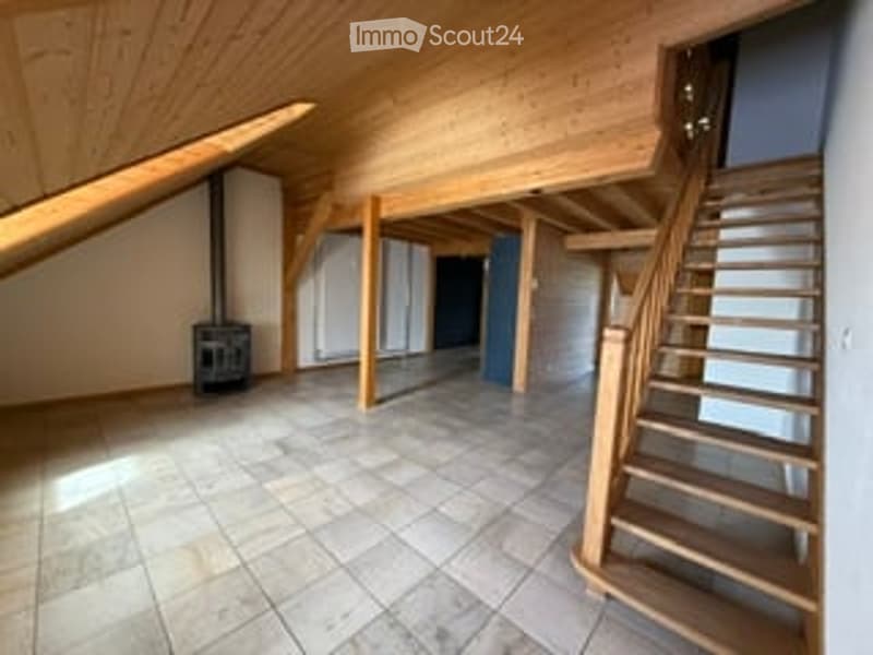 Bright, open attic space with wooden beams, tiled floor, and a staircase leading to another level. No furniture or equipment present.