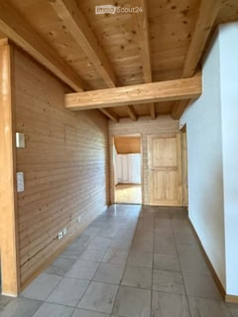 Empty hallway with wooden walls, exposed wooden beams on the ceiling, tiled floor, and a wooden door at the end.