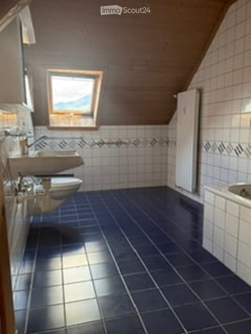 Modern bathroom with blue tiled floor, white tiled walls, a window, a sink, a toilet, and a bathtub.