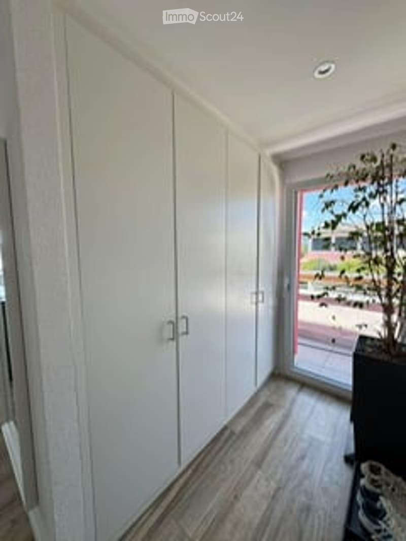 Empty room with white built-in wardrobes, wooden flooring, and a large window opening to a balcony with outdoor view.