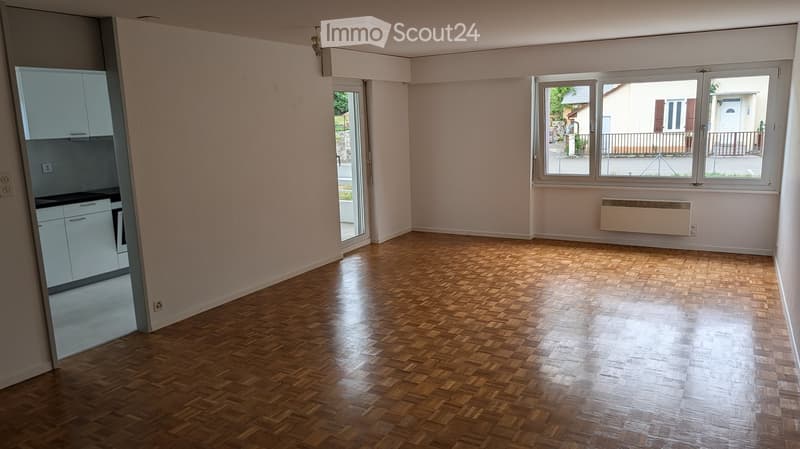 Empty room with wooden parquet flooring, white walls, large windows, and a sliding glass door leading to an outdoor area. The room is unfurnished and has a clean, minimalist design.