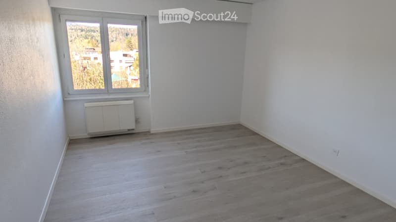Empty room with light wooden flooring, white walls, and a window with a view of the outdoors.