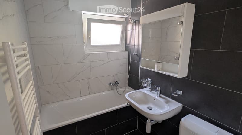 Modern bathroom with marble tiles, bathtub, sink, mirror cabinet, radiator, and toilet.