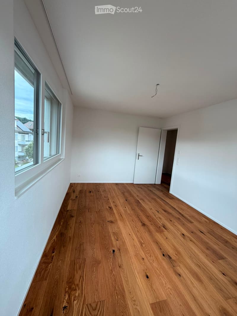 Empty room with wooden flooring, white walls, and large windows offering a view of the outside. There are two white doors leading to other areas.