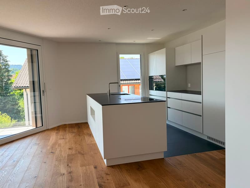 Modern kitchen with white cabinets, a central island, and a black countertop. Features a sink with a modern faucet, an oven, and large windows offering a view of the outdoors.