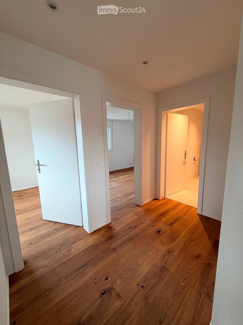 Empty hallway with wooden flooring, white walls, and three open doors leading to other rooms.