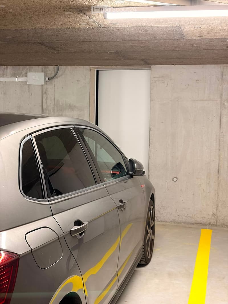 Underground parking area with a silver car parked in a designated spot, marked with yellow lines on the floor.