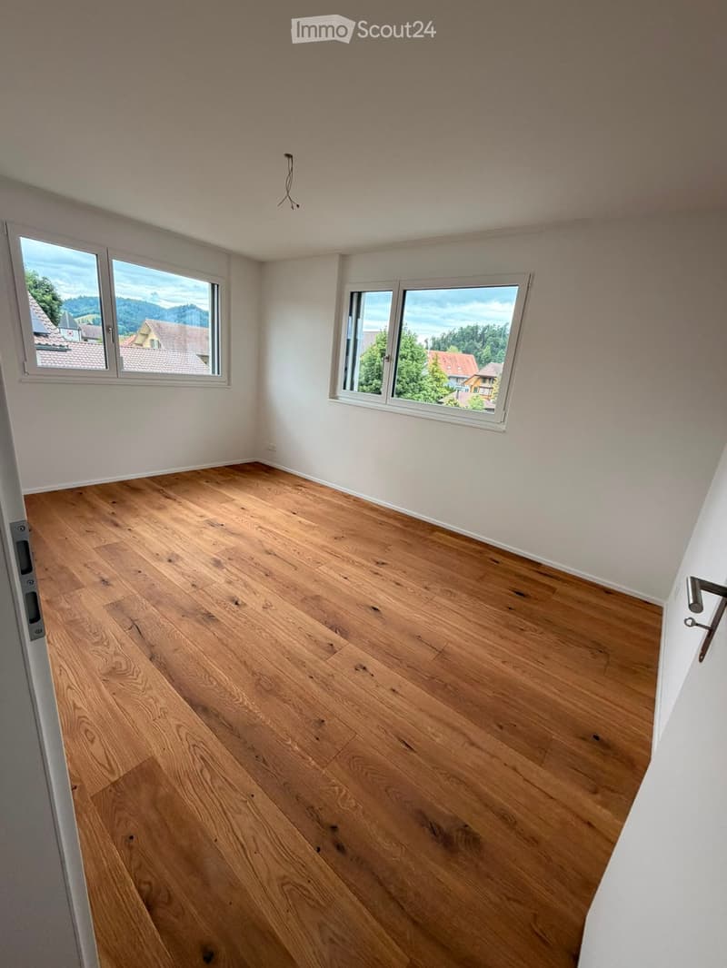 Empty room with wooden flooring and large windows offering a scenic view of the surrounding area.