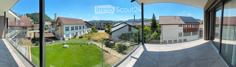 Modern balcony with glass railing, overlooking a well-maintained lawn and a residential neighborhood with houses and solar panels.