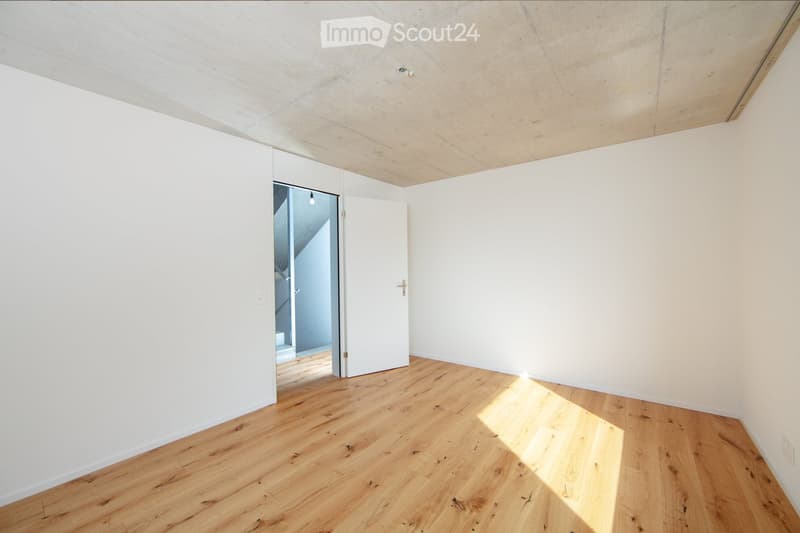 Empty room with white walls, wooden floor, and a white door leading to another space.