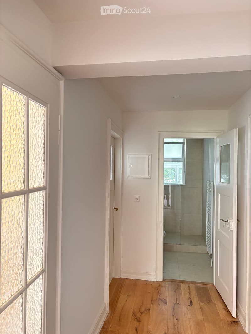 Empty hallway with light-colored walls, wooden flooring, and several doors leading to other rooms.