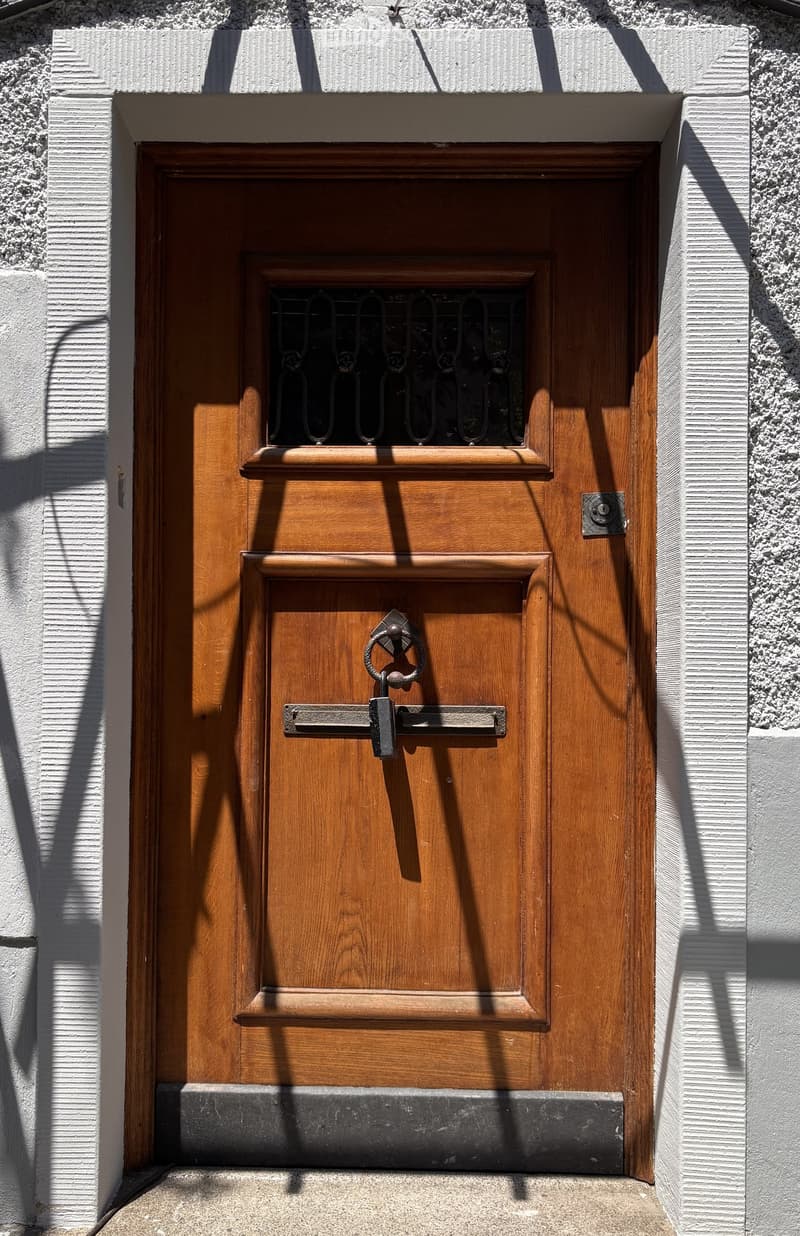 Wooden door with a small window and decorative metal handle, set in a white textured wall.