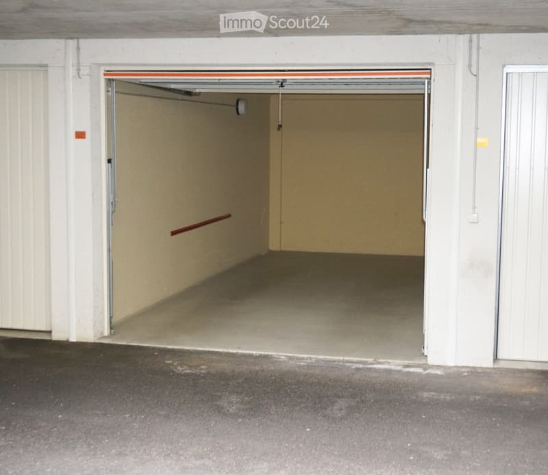 Empty underground parking space with a single open garage door, concrete walls, and a concrete floor.