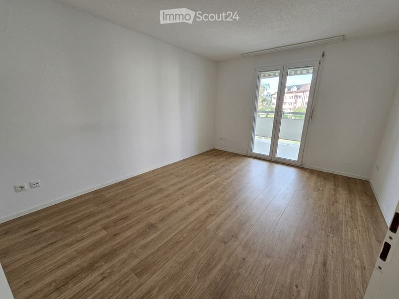 Empty room with wooden flooring and white walls, featuring a large sliding glass door leading to a balcony.