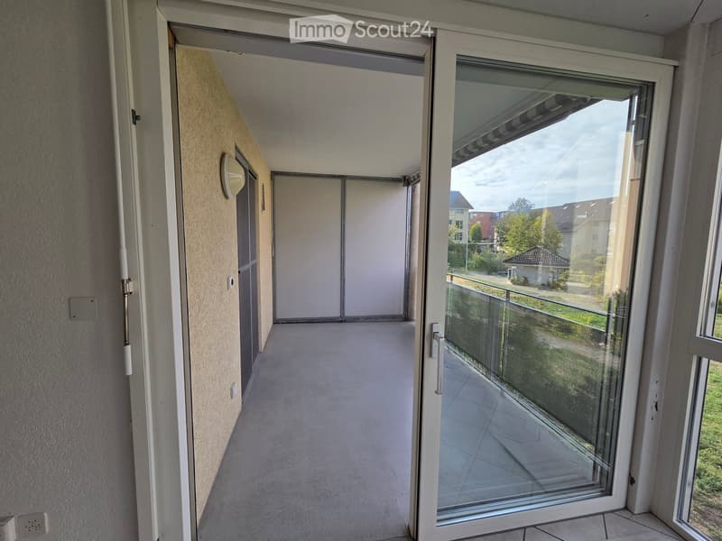 Balcony with glass sliding doors, tiled floor, and a view of the surrounding area including houses and greenery.