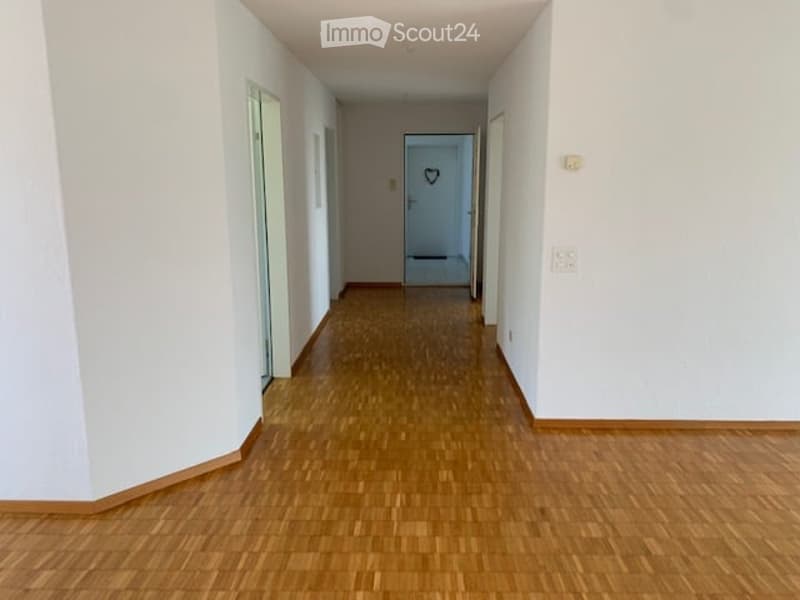 Corridor with wooden floors, white walls, closed doors, heart symbol above a door